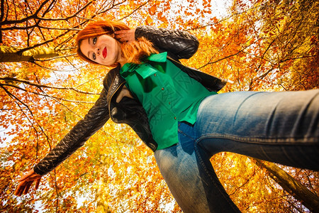 秋天公园年轻快乐女异常低角度视美丽的红头发女孩在户外飞行中放松图片