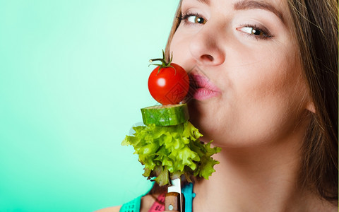 健美保和减肥概念运动健壮的女子身妇颈部有测量胶带在绿色蓝底背景上持有叉子和新鲜混合蔬菜工作室拍摄图片