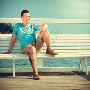 帅哥坐在码头的长椅上享受暑假的海边旅行时装和放松帅哥在码头旅游时装夏天图片