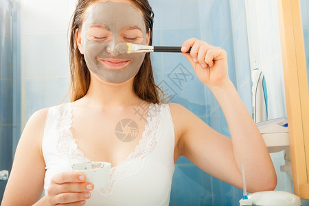 年轻女在浴室用面部灰色泥土遮面罩脸图片