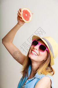 暑假快乐的滑稽女游客穿着太阳镜和帽子拿着葡萄果柑橘喝灰色水果上的汁图片