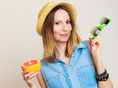暑假快乐的滑稽女游客穿着太阳镜和帽子拿着葡萄果柑橘喝灰色水果上的汁图片