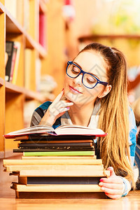在学校教育概念中穿着蓝眼镜的聪明女学生孩躺在大图书馆的地板上阅读书本图片