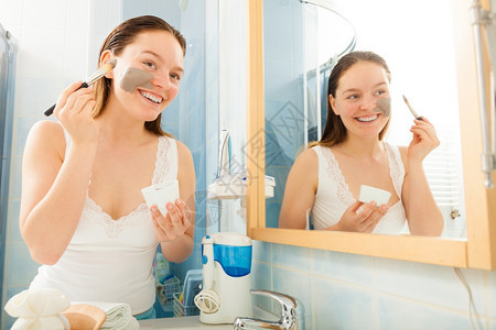 美容护皮肤化妆品和健康概念年轻女在浴室用泥脸部涂用面粘土罩顶着刷子和碗图片