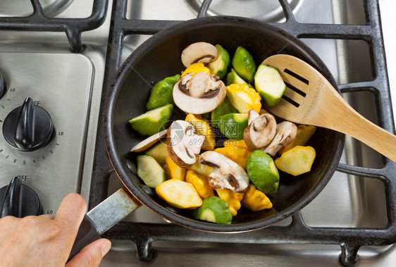 紧握着煎锅的手专注于食物同时用木勺搅拌蔬菜图片