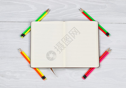开口笔记本的高角度视图新锋利的铅笔放在每个角落生锈的白色木制桌面上图片