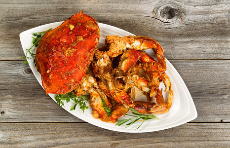 新鲜煮蟹的高角度视图上面有辣酱和白餐盘上的草药图片