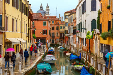 在雨天意大利伞下旅游者在威尼斯运河上行走图片