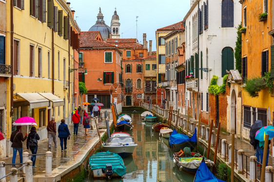 在雨天意大利伞下旅游者在威尼斯运河上行走图片