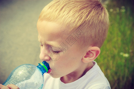 小口渴的男孩儿在户外用塑料瓶喝水图片