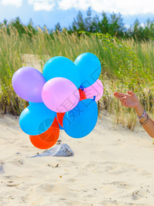 女手在沙滩丘背景户外拿着彩色气球图片