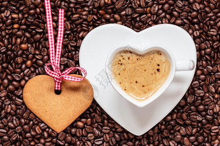 咖啡时间概念以咖啡豆背景上卡布奇诺莫和饼干姜的心形杯顶级视图图片