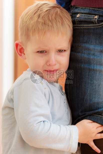 哭泣金发男孩子儿在家里拥抱着母亲的腿图片