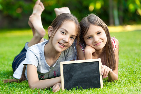 两个小女孩的肖像用空白黑板在草地上摆着图片