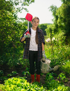 笑的姑娘在花园里装着铲子和水罐图片