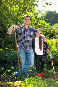 微笑的年轻父亲和女儿在花园装着铲子图片