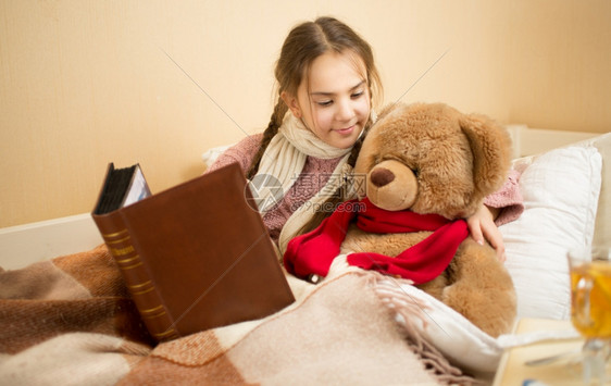在床上跟泰迪熊讲故事的可爱黑发女孩肖像图片