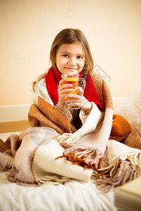 穿着毯子的可爱女孩肖像喝热茶床上加柠檬图片