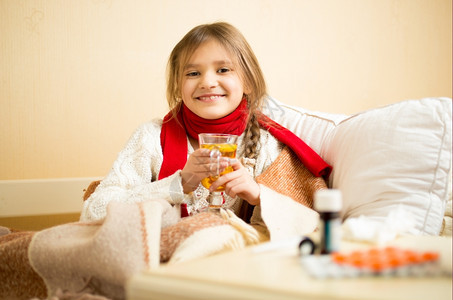 坐在床上喝热茶的可爱笑女孩肖像图片