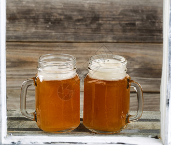 透过窗户看到两个玻璃罐子上面装满冰冷的啤酒图片