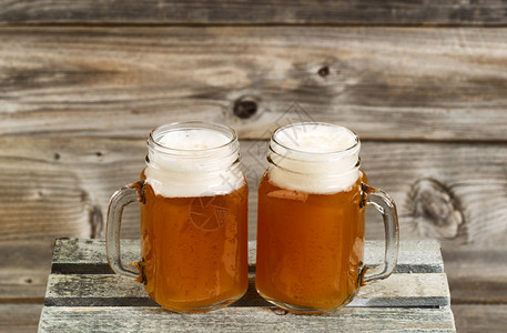 两罐装满冰冷的啤酒玻璃罐子放在木箱顶上底有生锈的木头图片