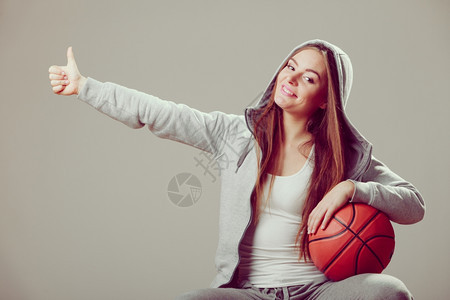 成功的运动少女穿着戴头罩的运动衫拿着大拇指手势的篮球图片
