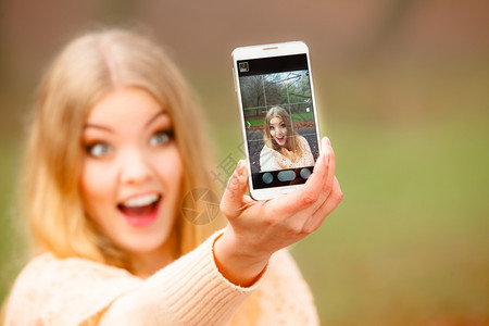 科技互联网和幸福概念女内容孩在秋季公园户外散步时用智能手机相拍摄自图片
