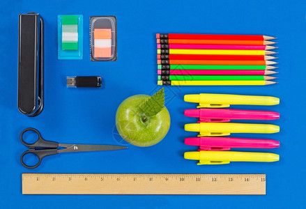 办公室或返回学校用品包括绿色苹果亮点标记订书机拇指驱动器标尺剪刀制表符和蓝底彩色铅笔图片