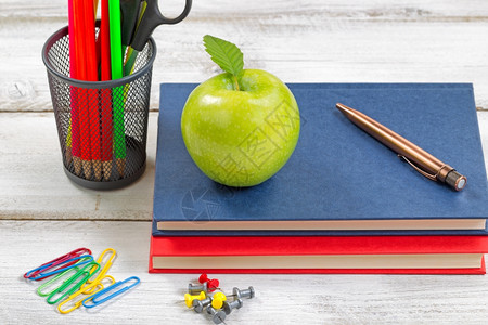 健康的绿苹果书籍笔纸剪片和容器在白色桌面上装有用品图片