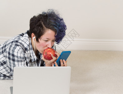 女孩一边吃苹果看手机前面有电脑一边躺着听家里的音乐图片