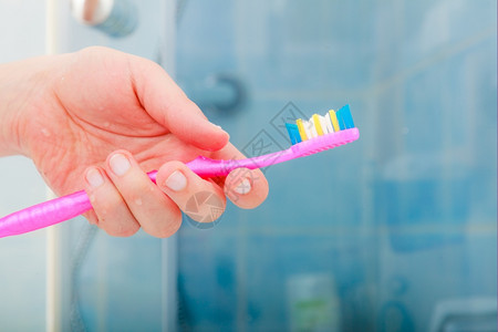 口腔健康概念近身女用手在浴室里拿着粉红色牙刷图片