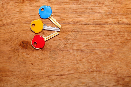 木制表格背景上三把有多彩塑料外衣盖的家用钥匙图片
