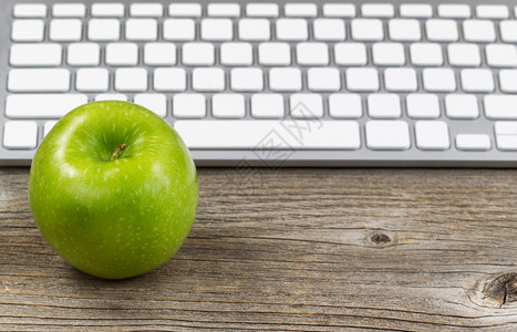 选择地关注成熟的绿苹果并在背景中部分键盘在生锈木上以水平格式布局图片