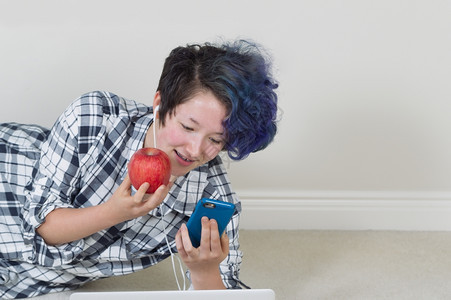 年轻女孩拿着苹果一边看手机前面有电脑一边躺着听家里的音乐图片