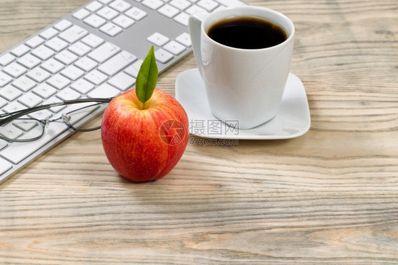 用电脑键盘贴上红色苹果在桌面上以背景阅读眼镜和咖啡杯图片