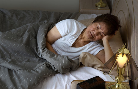 无休止的老年妇女晚上盯着床位看失眠的概念图片