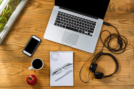 工作桌面包括膝上型电脑耳机笔记本咖啡手机和有角日光窗的苹果图片