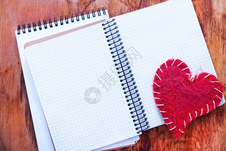 红心背景木制桌上的红桃和笔记背景