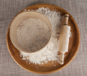 在木盘上的面粉打滚针和筛子在美丽的桌布上作成关于烹饪美食的杂志照片图片