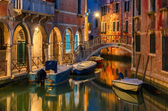 夜间在威尼斯的横向运河和行人桥有街道灯光照亮的桥和房屋有停靠船只意大利图片