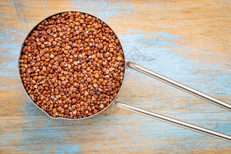 以木本为底的金属测量杯中无蛋白红quinoa谷物图片