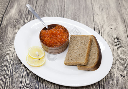 鲜开胃的红鲑鱼子酱放在木罐中瓷盘上放着面包片图片