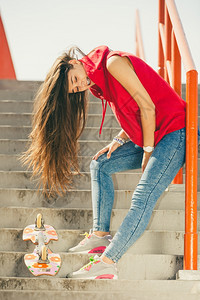 城市滑板女孩穿着的酷长发女孩穿着滑板的酷女孩靠在城市楼梯上扶手图片