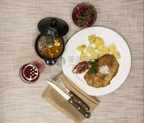 PetiteWienerschnitzel配有煮土豆和番茄酱身着白色瓷板用叉子和刀在木制背景上甜菜沙拉和番茄红辣椒汤橄榄油酱迷迭图片