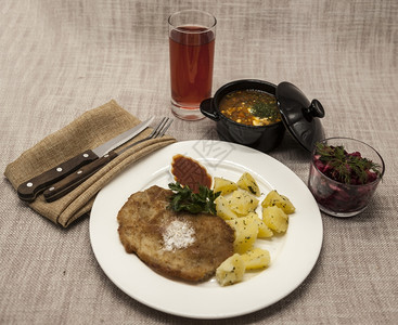 PetiteWienerschnitzel配有煮土豆和番茄酱身着白色瓷板用叉子和刀在木制背景上甜菜沙拉和番茄红辣椒汤橄榄油酱迷迭图片