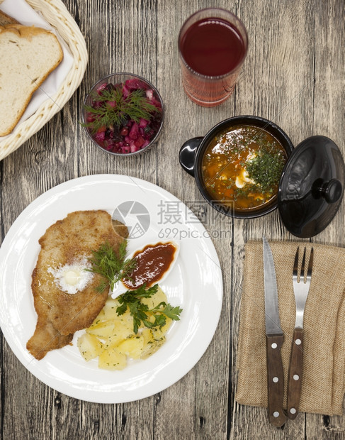 PetiteWienerschnitzel配有煮土豆和番茄酱身着白色瓷板用叉子和刀在木制背景上甜菜沙拉和番茄红辣椒汤橄榄油酱迷迭图片