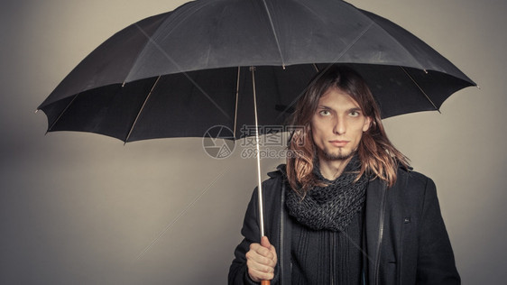 穿着黑色大衣的英俊时尚男子肖像和拿着雨伞的围巾图片