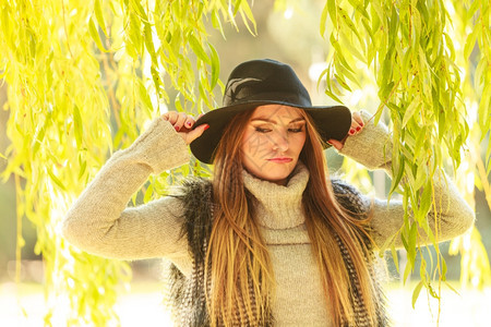 可爱的美女穿着黑色帽子毛皮腰衣的围着公园柳树的叶子图片
