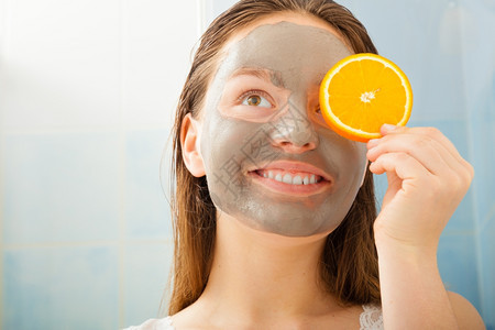 美容护肤化妆品和健康概念戴面部粘土罩的年轻妇女在浴室里用橘子水果切片遮住眼睛图片