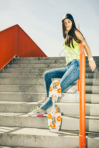 酷的长发女孩滑板坐在城市栏杆上活跃的生方式在夏天很怪异图片